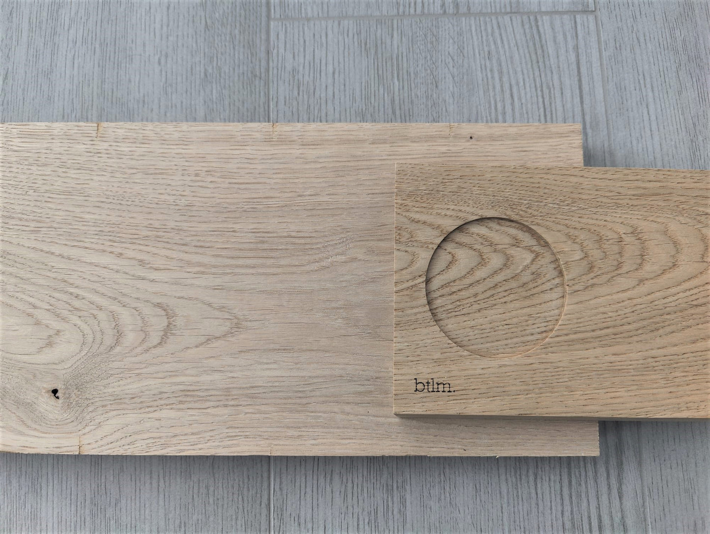 Front view of wooden oak serving board, slightly offset right, displayed alongside the original wooden plank it was crafted from.